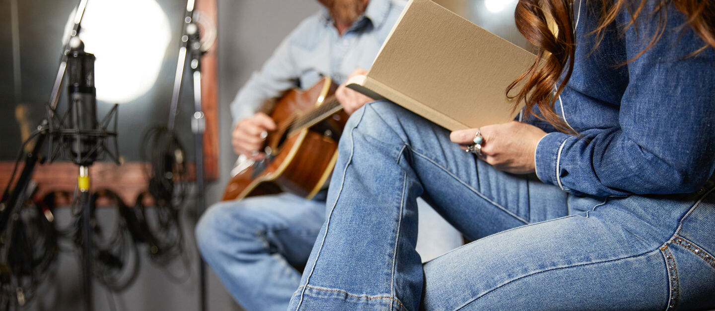 A woman holding a notebook and a man playing guitar with faces out of the photo.